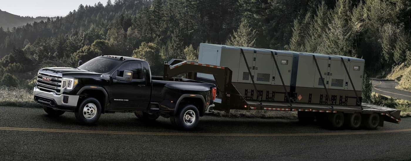 Side angle view of a black 2022 GMC Sierra 3500 HD towing heavy machinery.