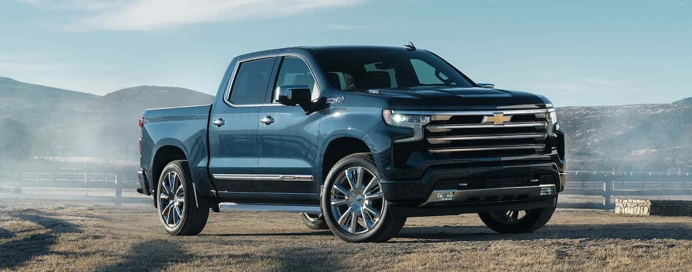 A blue 2022 Chevy Silverado 1500 High Country, a popular used truck for sale, is shown parked on a farm.