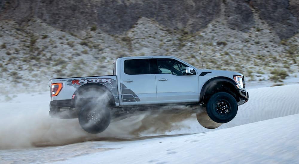 A silver 2023 Ford F-150 Raptor R is shown from the side while jumping over a sand dune.