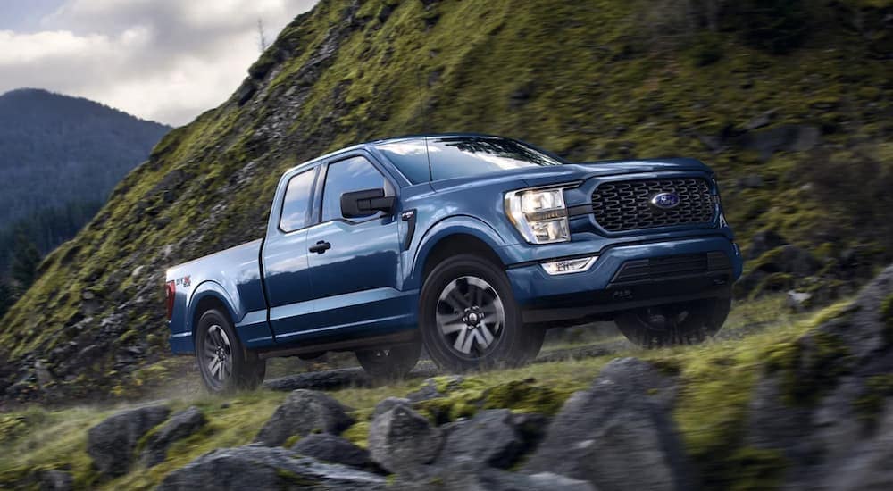 A blue 2022 Ford F-150 is shown off-roading in the mountains.