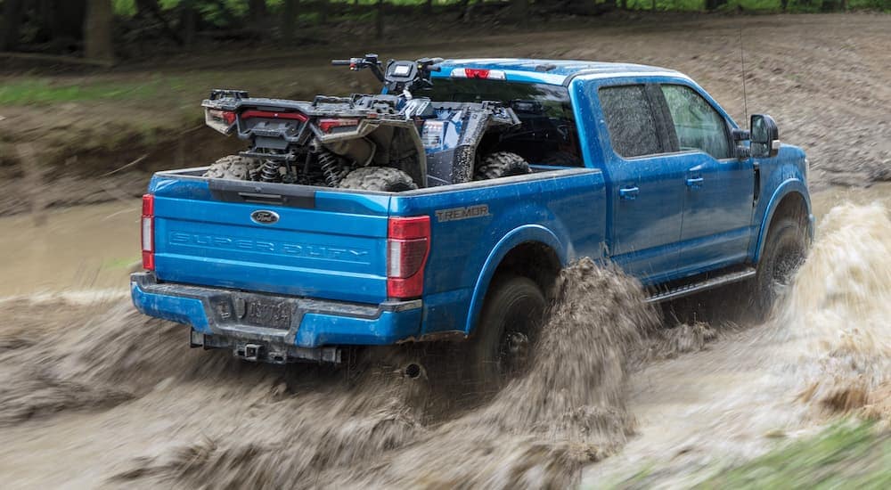 A blue 2021 Ford F-250 Tremor is shown hauling an ATV through mud after leaving a used truck dealer near DeWitt..