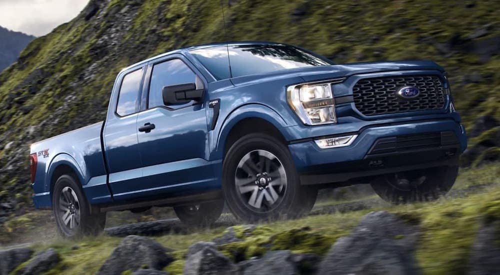 A blue 2023 Ford F-150 is shown from the side driving on a mountain.