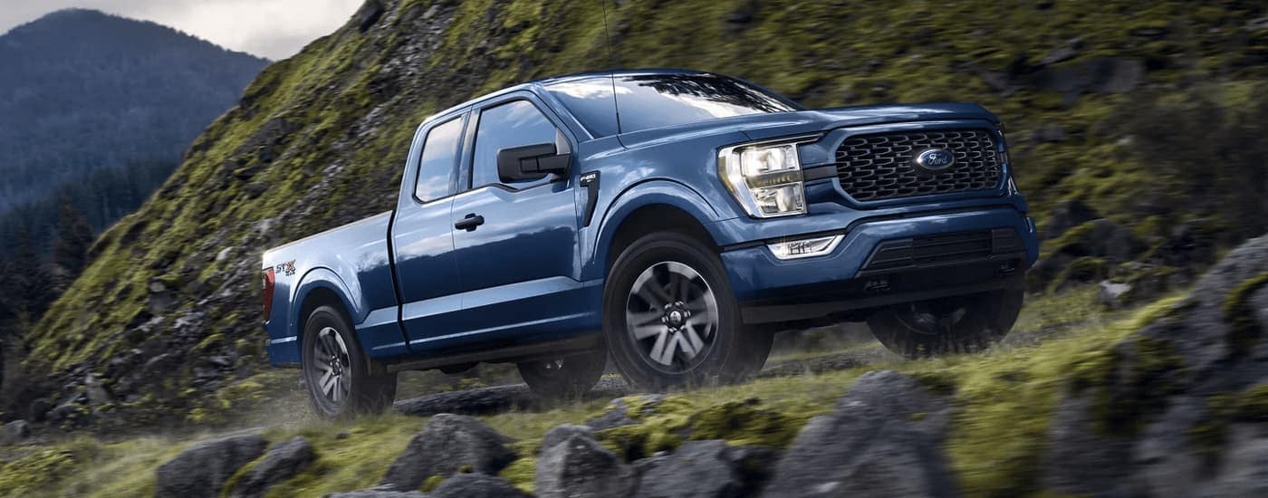 A blue 2023 Ford F-150 STX is shown driving on a steep rocky mountain road.