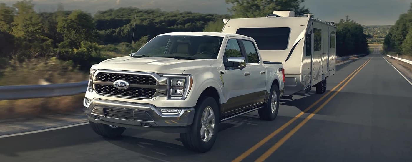 A white 2023 Ford F-150 is shown towing a camper trailer after leaving a Ford dealership in Central Michigan.
