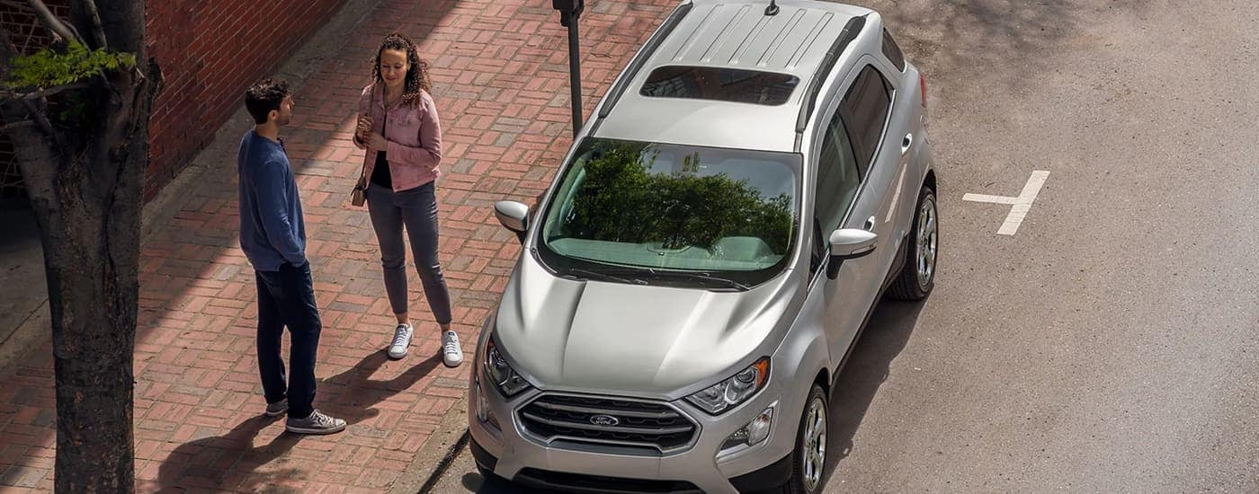 A silver 2022 Ford EcoSport is shown parked on a city street near a Lansing Ford dealer.