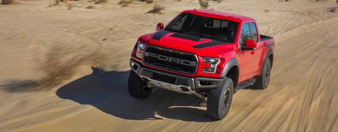 A red 2020 Ford F-150 Raptor is shown from the front off-roading through a desert.