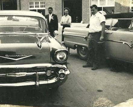 men standing outside two cars