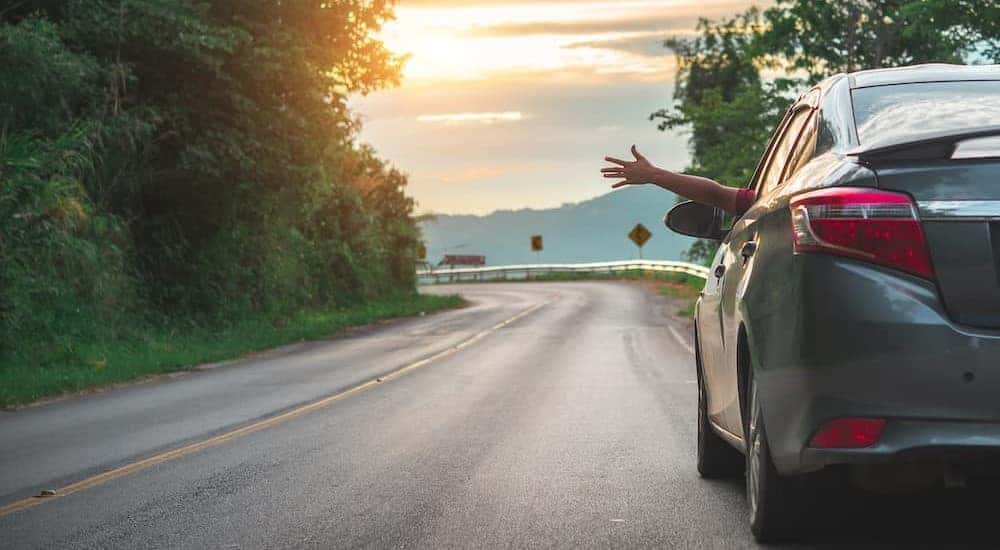 A hand is shown waving out of a car window.