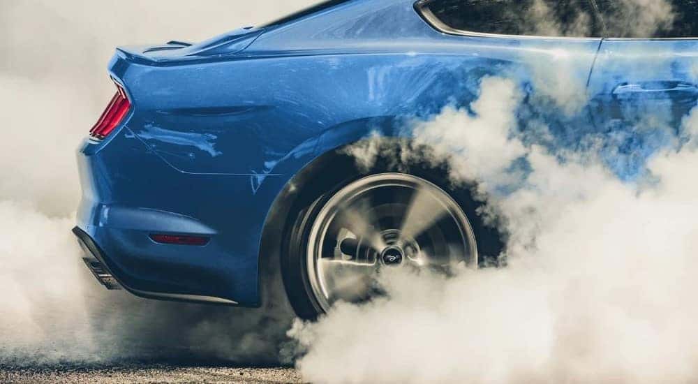 A close up shows a blue 2021 Ford Mustang doing a burnout.