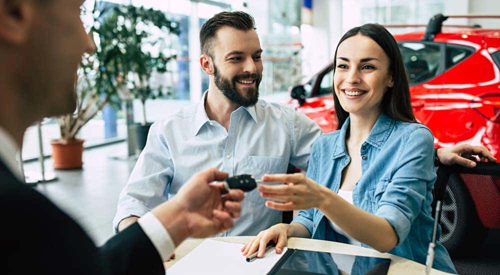A couple is shown accepting car keys from a salesperson.