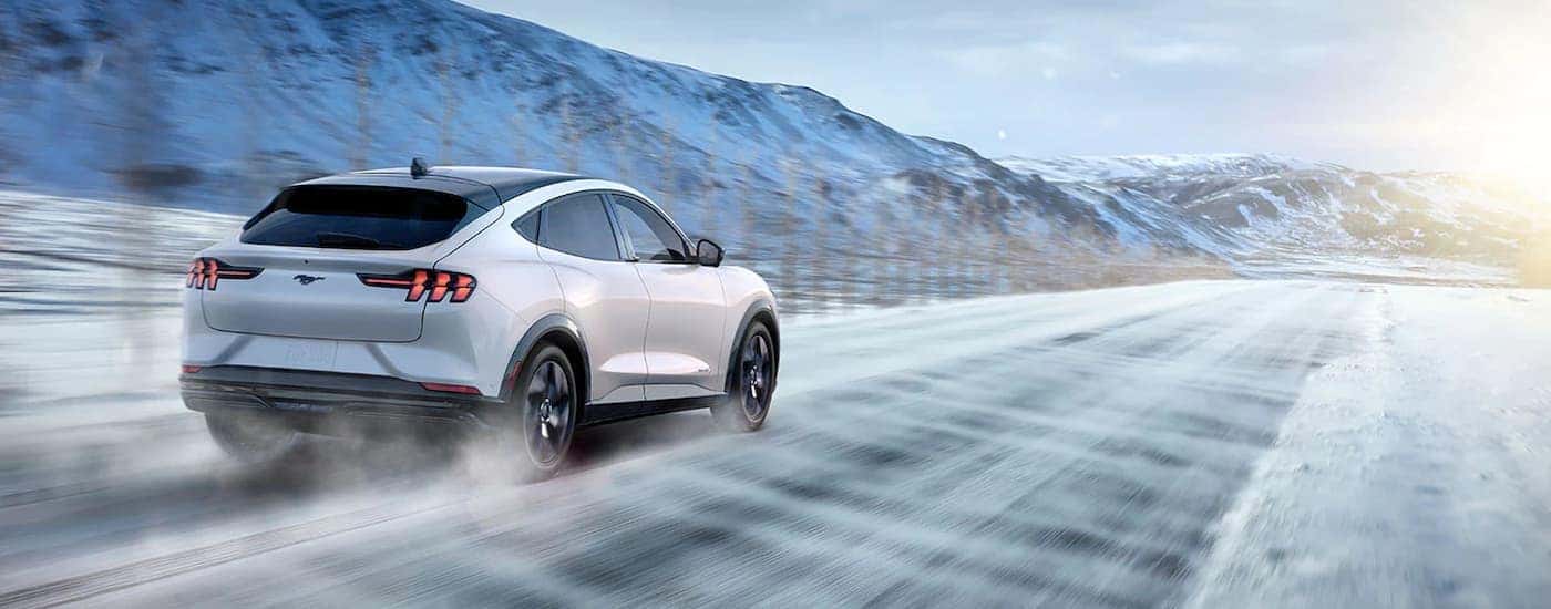 A white 2022 Ford Mustang Mach-E Premium is shown from behind driving on a snowy road.
