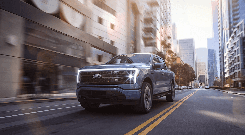 A light blue 2022 Ford F-150 Lightning is shown driving down a city street after leaving a Zionsville Ford dealer.