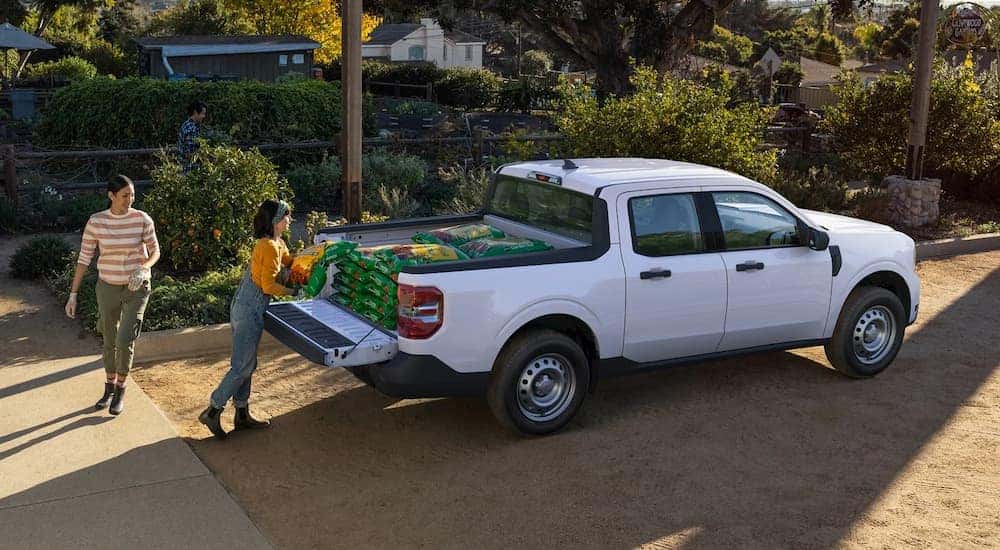 Two people are shown stacking potting soil into the bed of a white 2022 Ford Maverick.