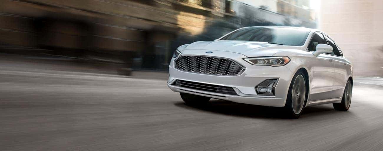 A white 2020 Ford Fusion is shown speeding down a city street.