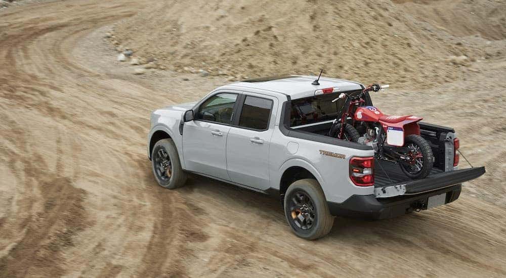 A grey 2023 Ford Maverick Tremor is shown from the rear while hauling a dirt bike off-road.