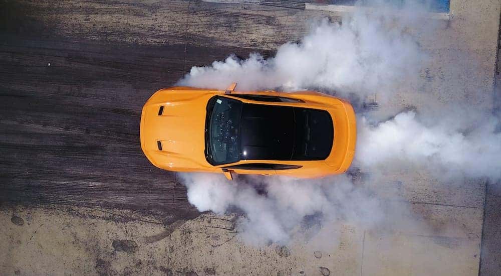 An orange 2017 Ford Mustang GT is shown from a high angle surrounded by smoke.