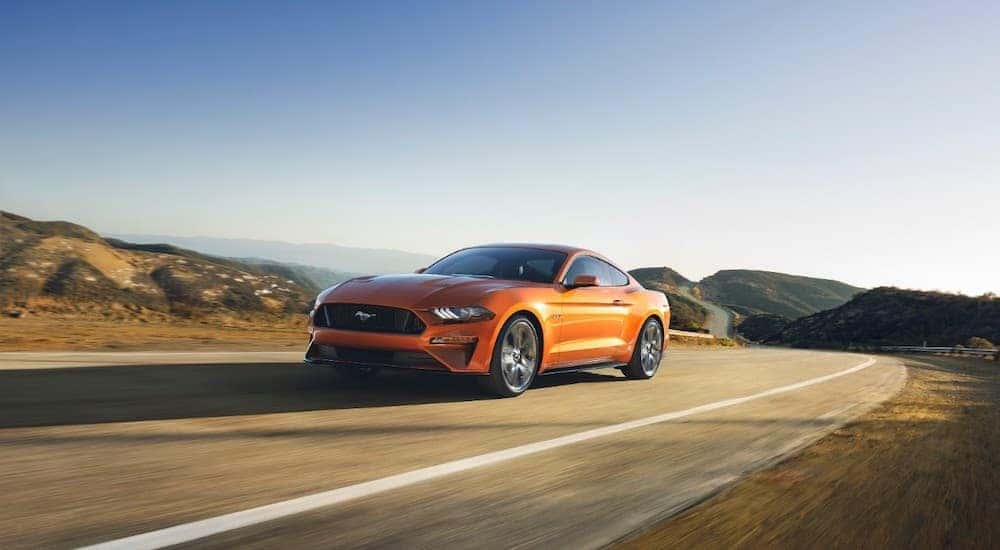 An orange 2018 Ford Mustang is shown driving on an open road after leaving a used Ford dealer.