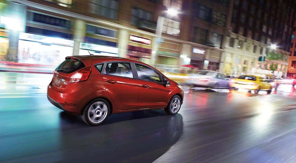 A red 2018 Ford Fiesta is shown from the side while driving on a city street.