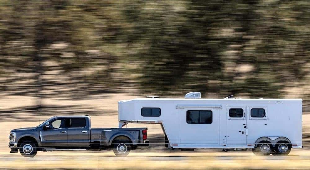 A grey 2023 Ford F-350 Lariat is shown from the side towing a trailer.