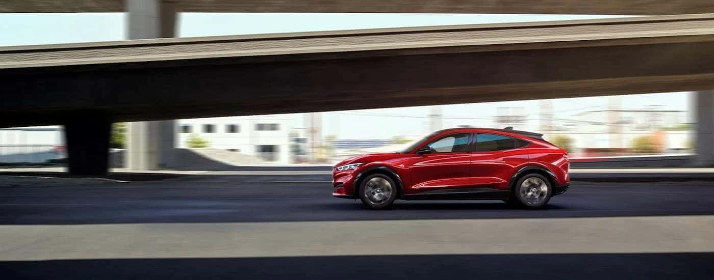 A red 2023 Ford Mustang Mach-E is shown from the side driving on a highway.