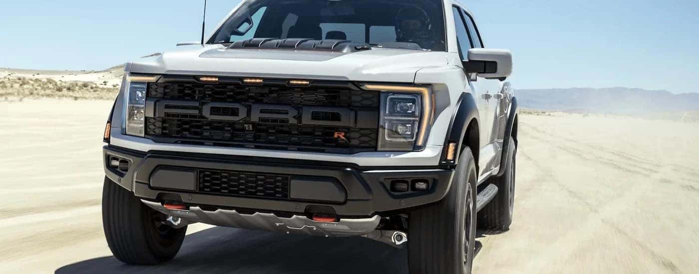 A white 2023 Ford F-150 Raptor R is shown from the front driving through a desert.