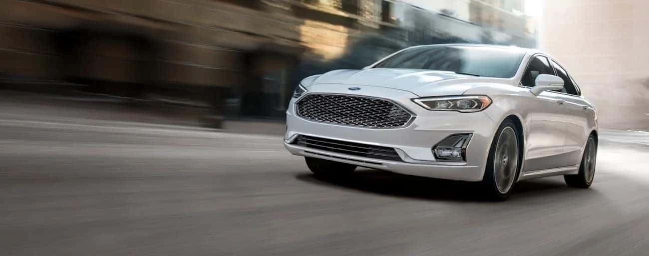 A white 2020 Ford Fusion is shown speeding down a city street.