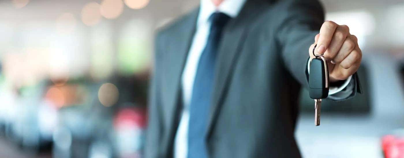 A salesman is shown holding a set of car keys at a used car dealer.