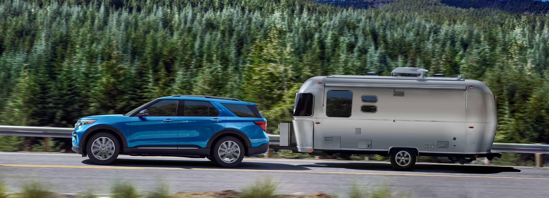 Blue 2021 Ford Explorer hauling a silver camper through a forest
