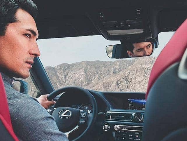 A man sits with his hand at the steering wheel of a Lexus vehicle with a mountain view through the window.
