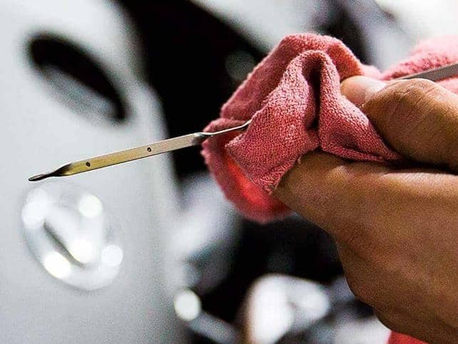 A Lexus service worker uses a pink towel to wipe an oil check rod.