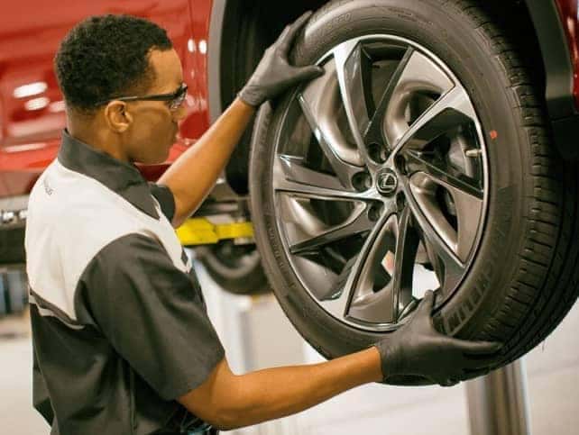 A service rep rotates a tire on a red Lexus.