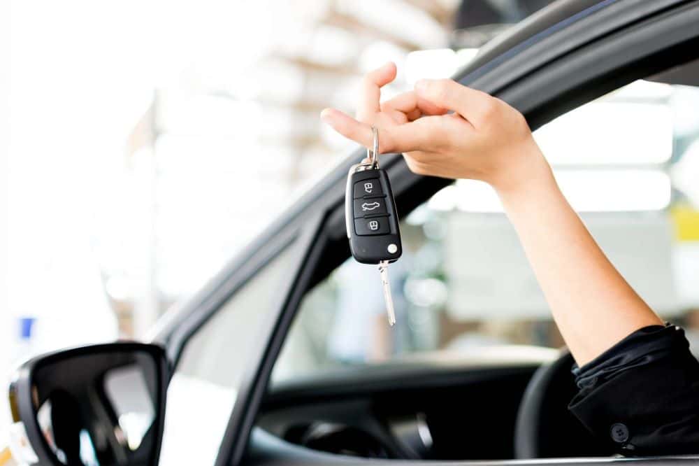Image of hand held out of car window, holding car key