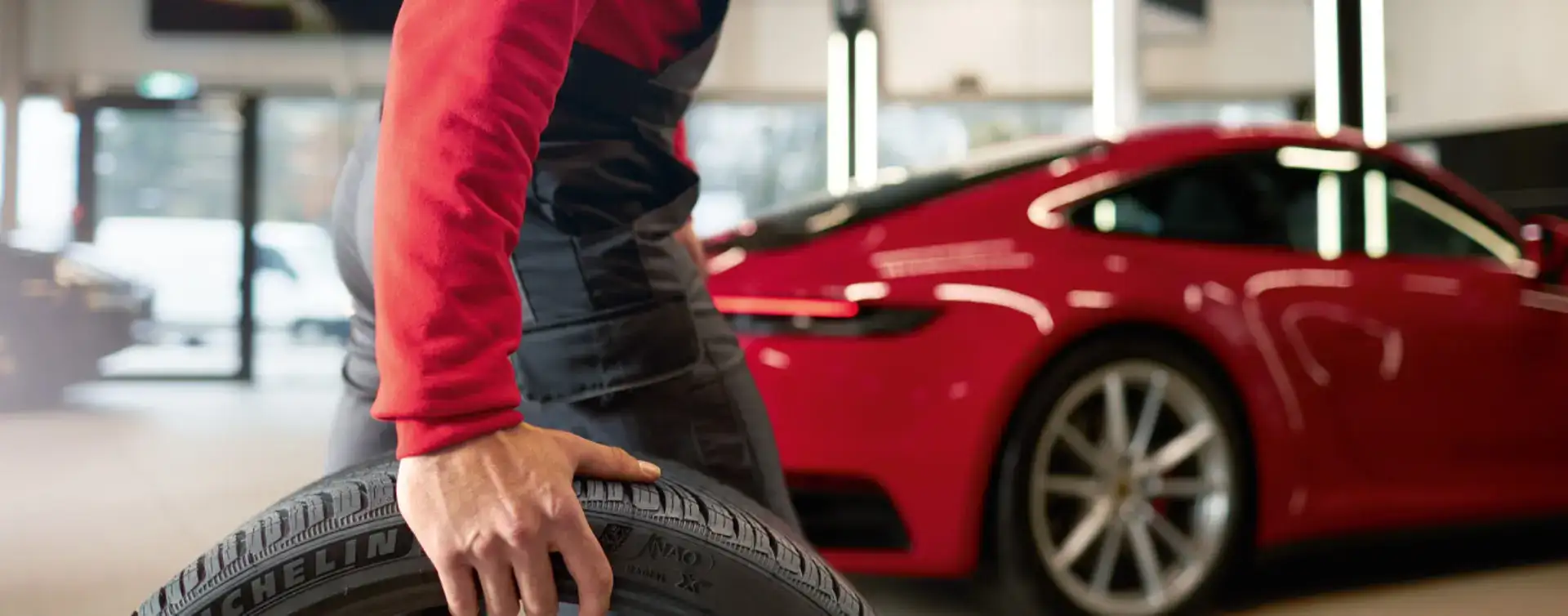 Mechanic with a tire and a red Porsche in the background