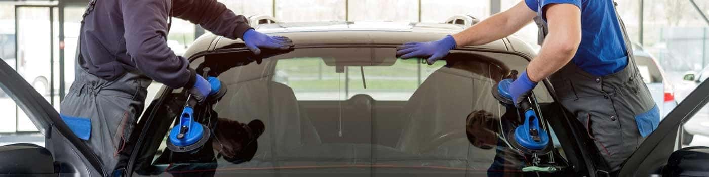 Two service techs replacing the windshield wipers on a vehicle