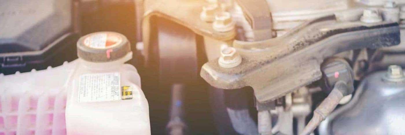 Close up view of a bottle of engine coolant next to an engine