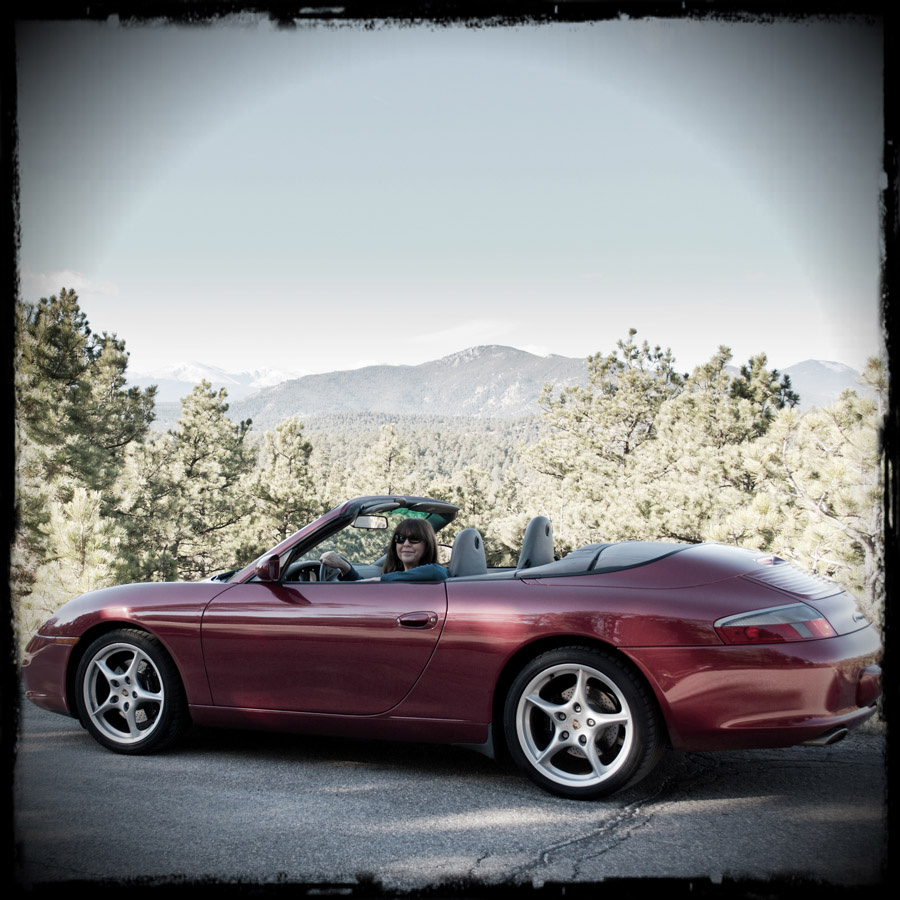 Roxanne sitting in her Porsche 911 Cabriolet, parked on the shoulder of a mountain road.