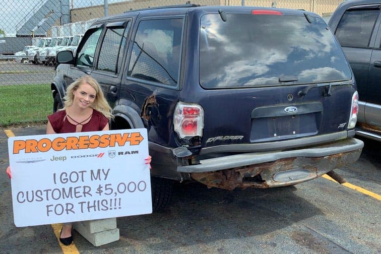 smiling Progressive customer kneeling next to the trade-in SUV they received $5000 for