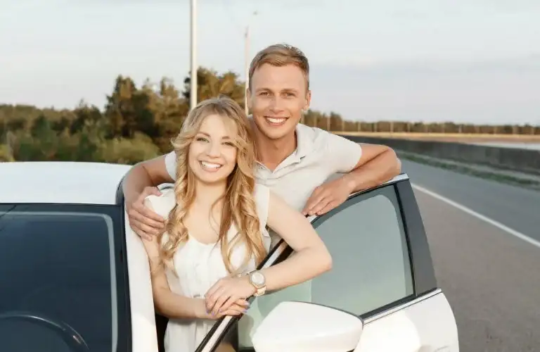 young couple standing outside of white car smiling