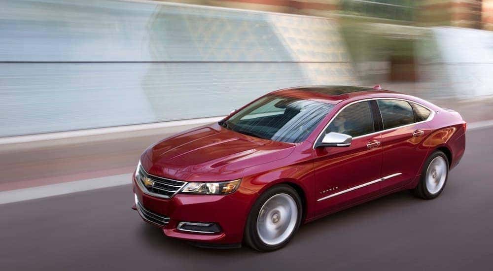 A red 2018 Chevy Impala driving on a city highway near a local Chevy dealership in Bethleham, PA.