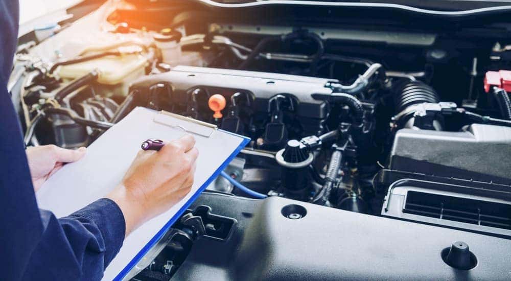 A Bethlehem, PA, mechanic is holding a clipboard while looking at the engine bay of a used car.