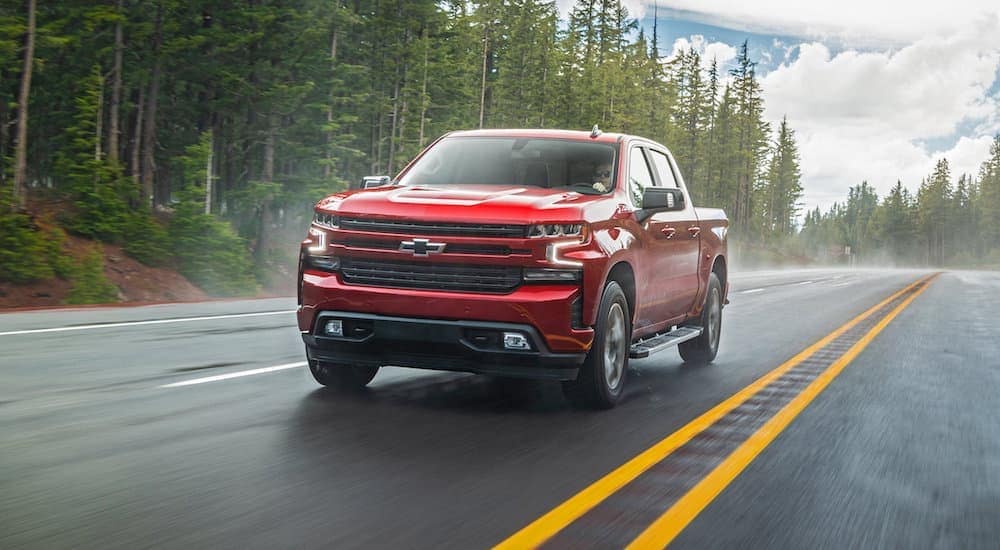 A red 2020 Chevy Silverado 1500 is driving on a wet road.
