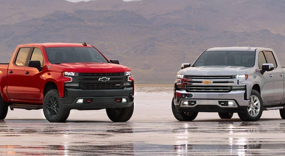 A red 2020 Chevy Trailboss and a silver 2020 Chevy Z71 are parked in a large parking lot with mountains in the distance. 