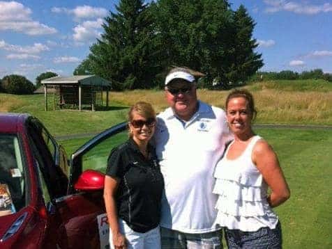 A man and two women taking a photo in front of a car