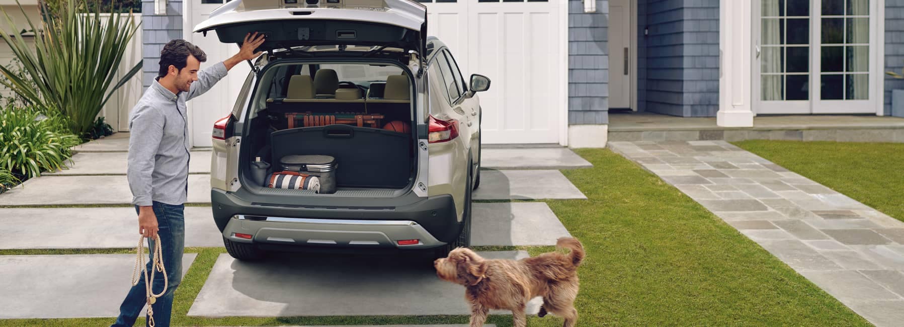 A man and his dog loading up the back of a 2021 Nissan Rogue parked in residential driveway