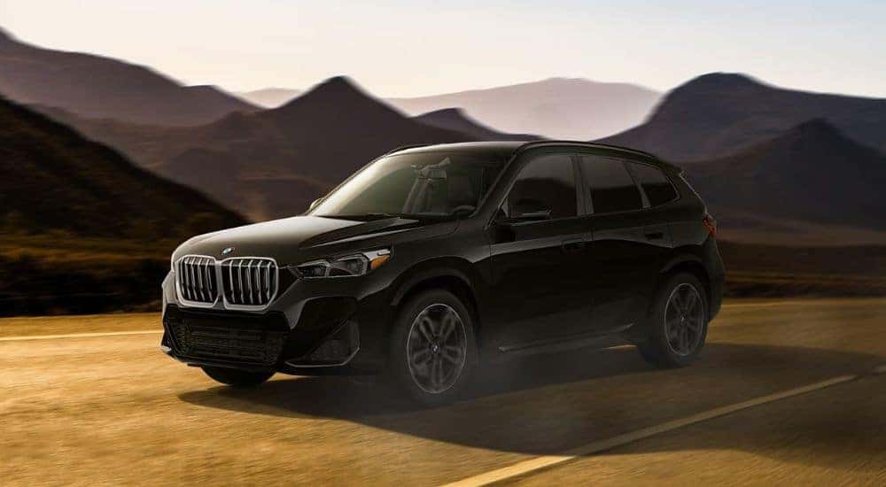 A black 2024 BMW X1 is shown driving past mountains after leaving a BMW dealer near Dallas.