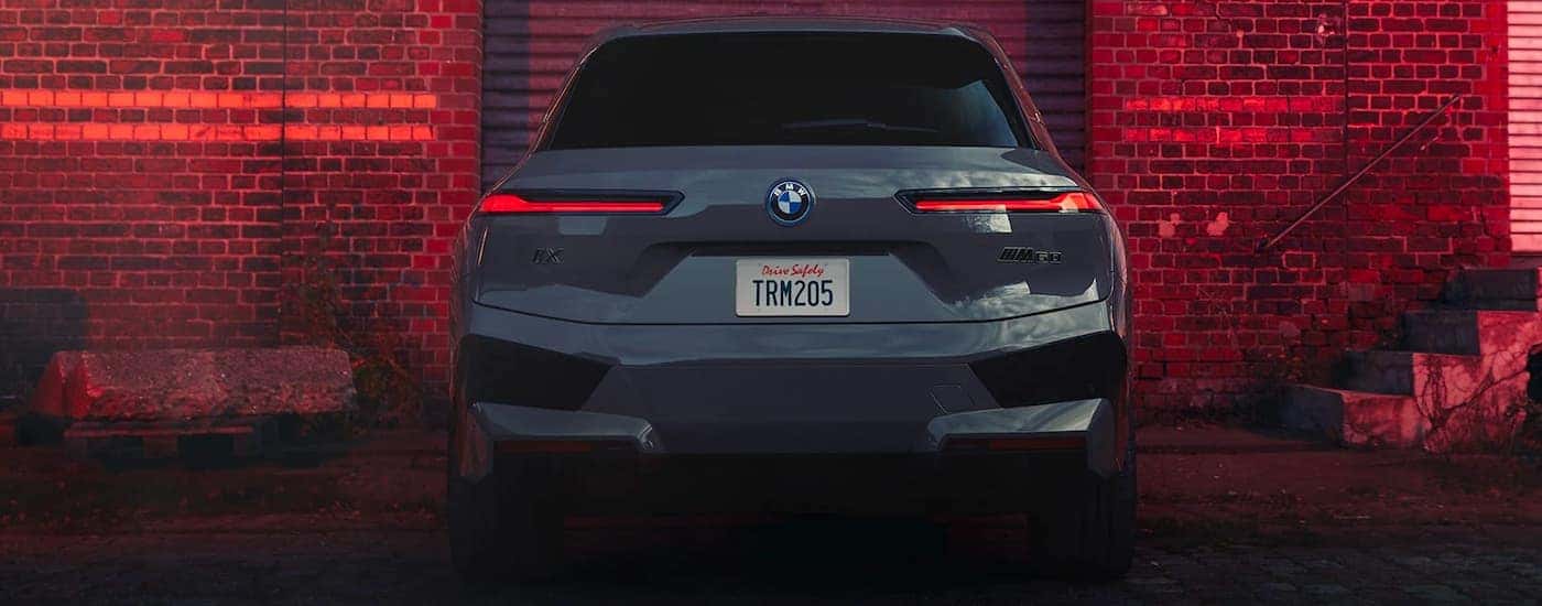 A grey 2022 BMW iX M60 is shown from the rear in front of a brick wall.