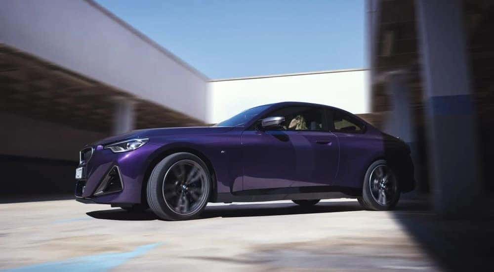A purple 2024 BMW M240i is shown driving at a parking garage.