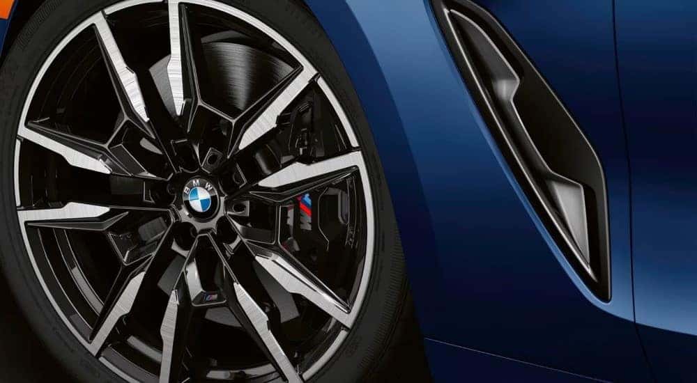 A close up shows a chrome and black rim on a blue 2024 BMW M850i.