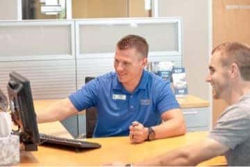 A man sitting inside a dealership, pointing at his computer.