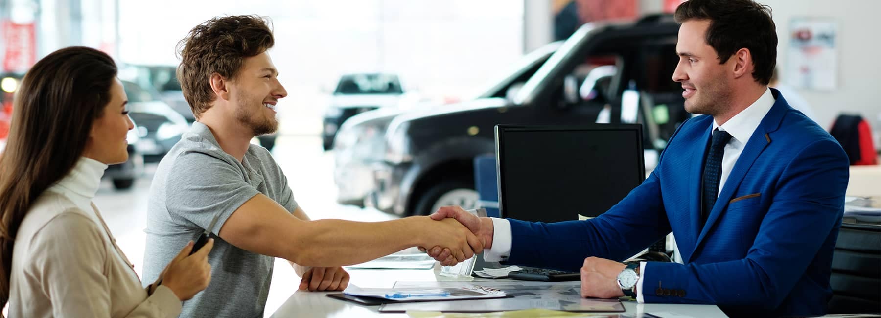 A customer and a car salesman shake hands after a car purchase